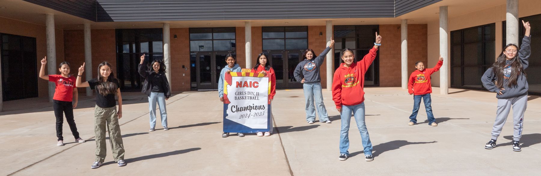 School girls proudly pose as basketball champions in front of their school building, celebrating the 2024-2025 season.