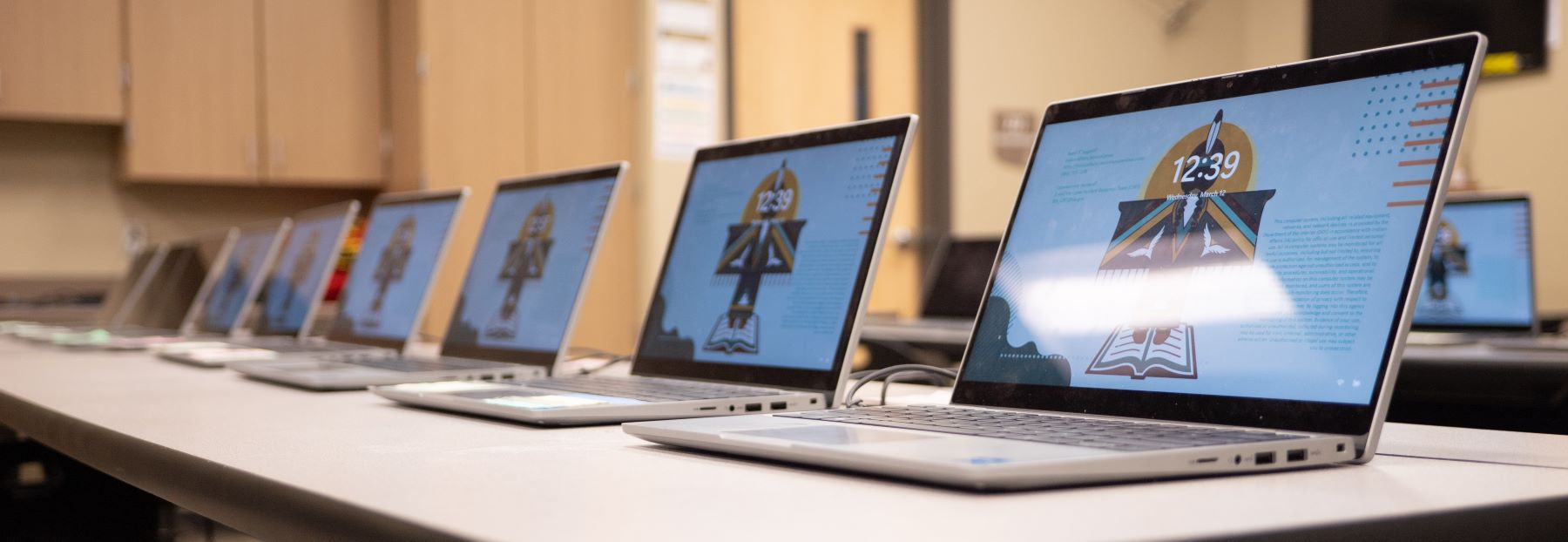 A row of several laptops neatly arranged on a table in a school setting.