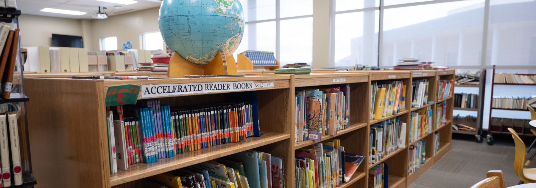 A school library featuring shelves filled with books and a globe prominently displayed among them.