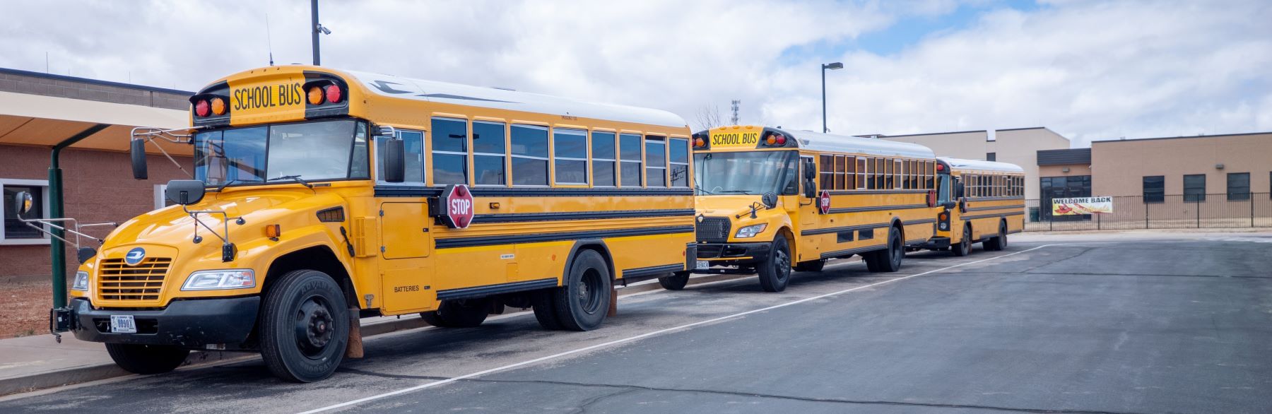 Three school buses lined up outside school waiting to pick up students.